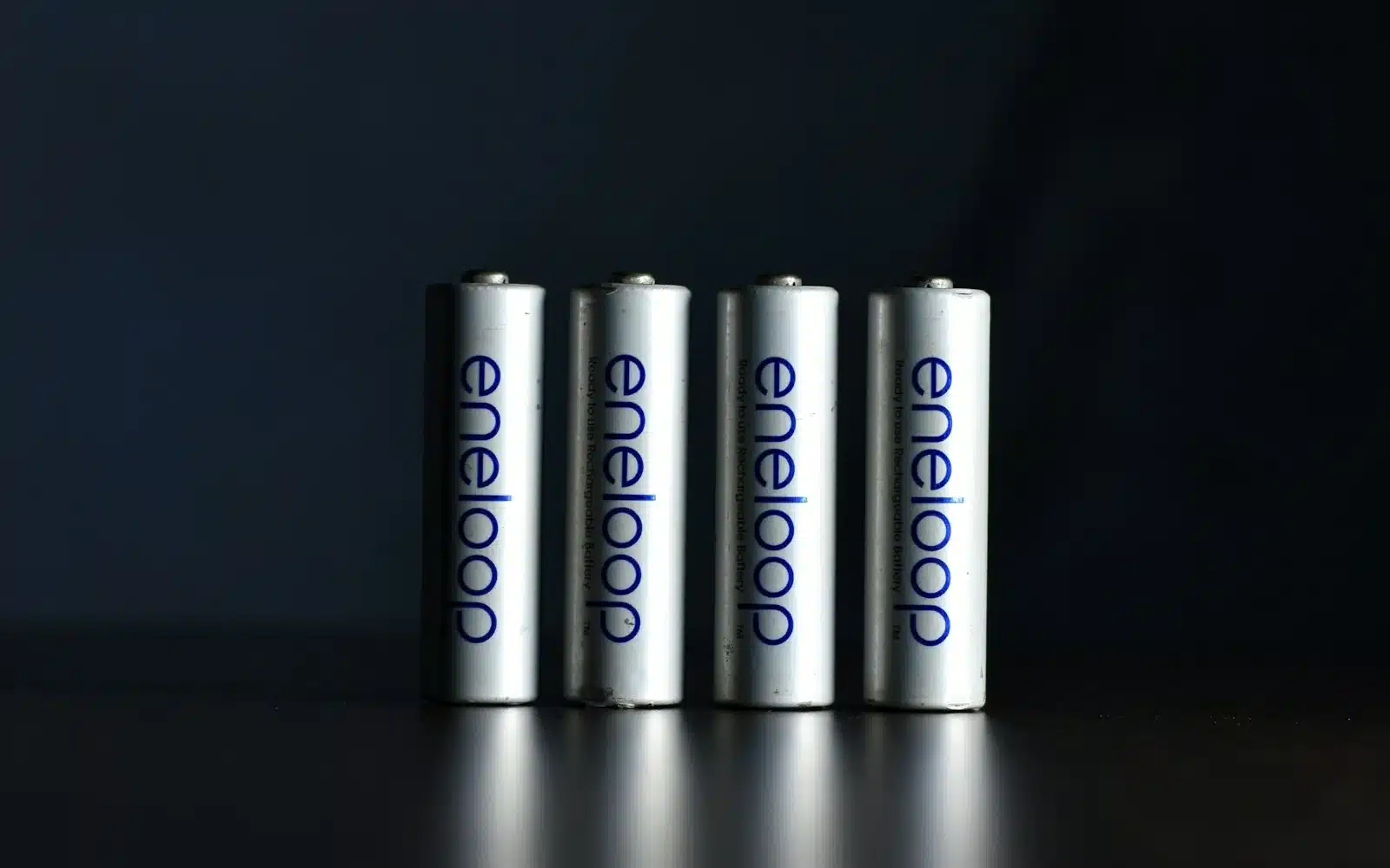Four white Panasonic Eneloop rechargeable AA batteries standing on a dark surface