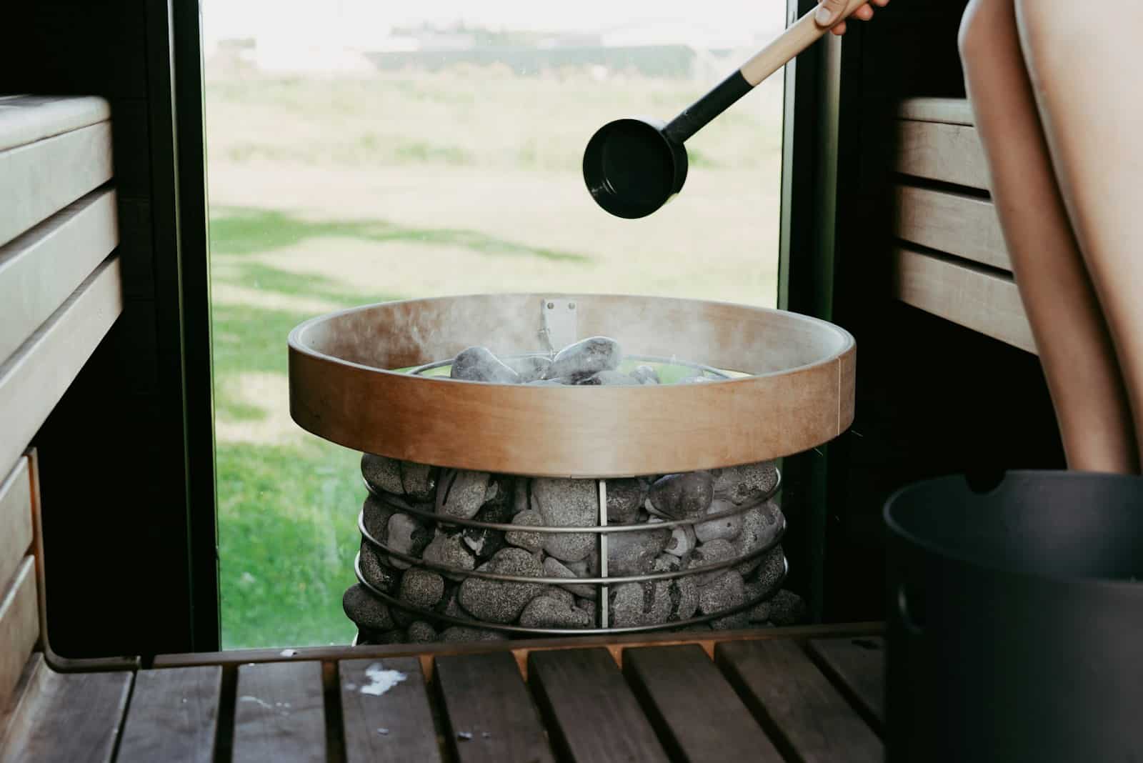 Water being poured onto hot sauna stones creating steam in a wooden Finnish sauna