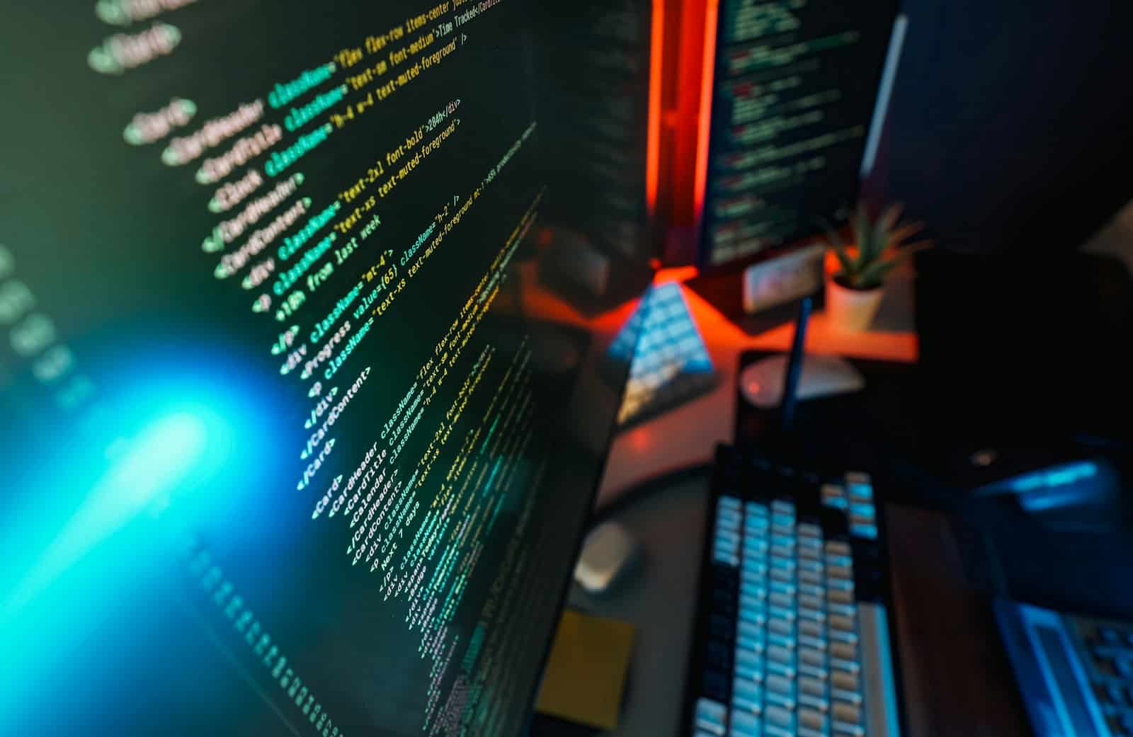 Developer workspace with a colorful code editor on a screen lit by ambient blue and red lighting