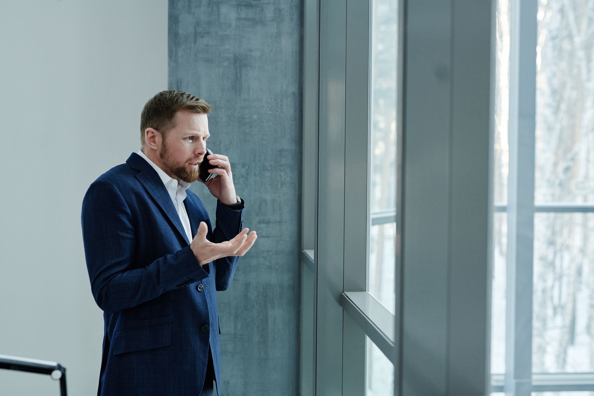 Real estate agent in a blue suit on the phone with a client by an office window
