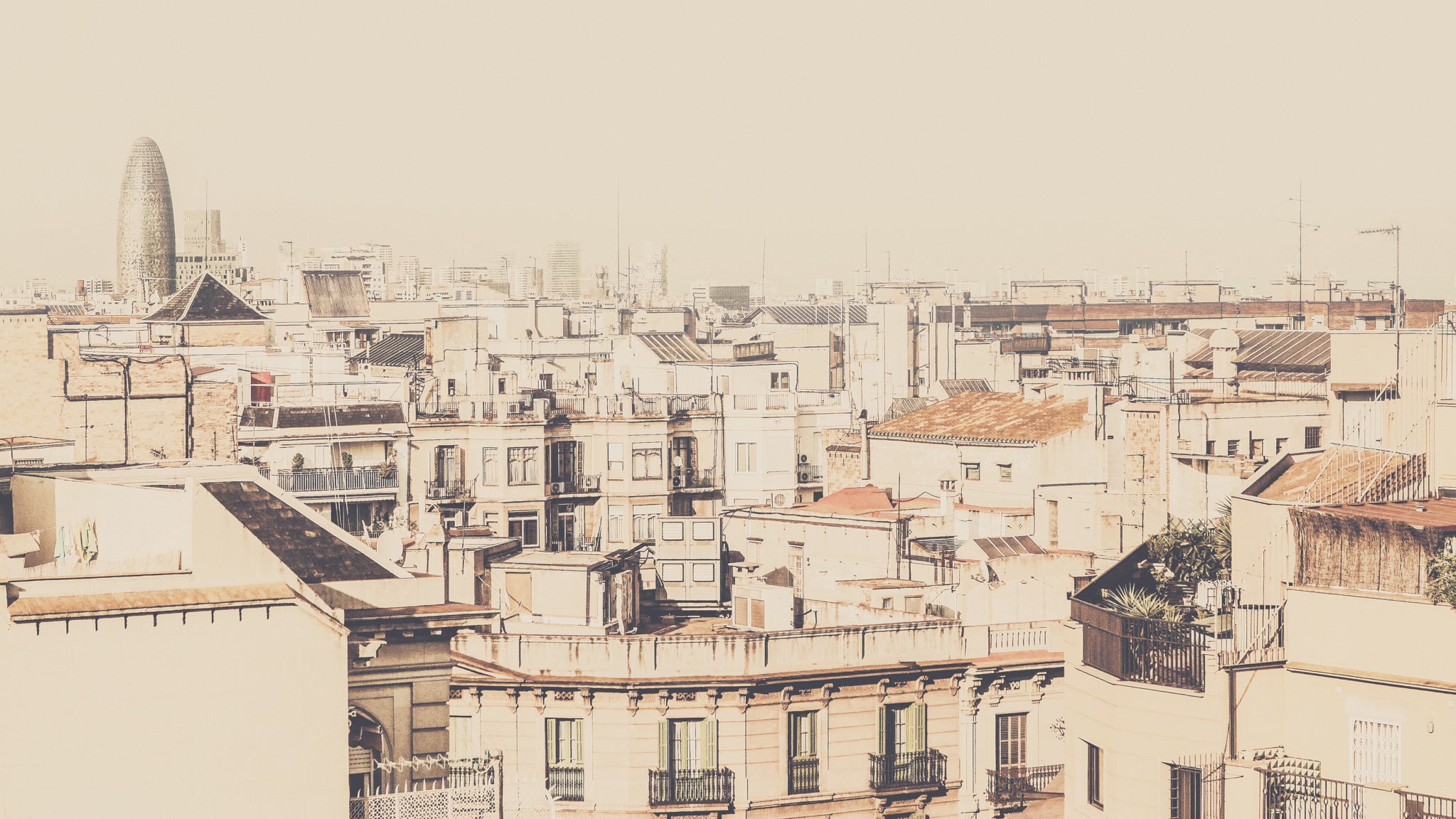 Densely packed rooftops and apartment blocks across central Barcelona with Torre Glories behind