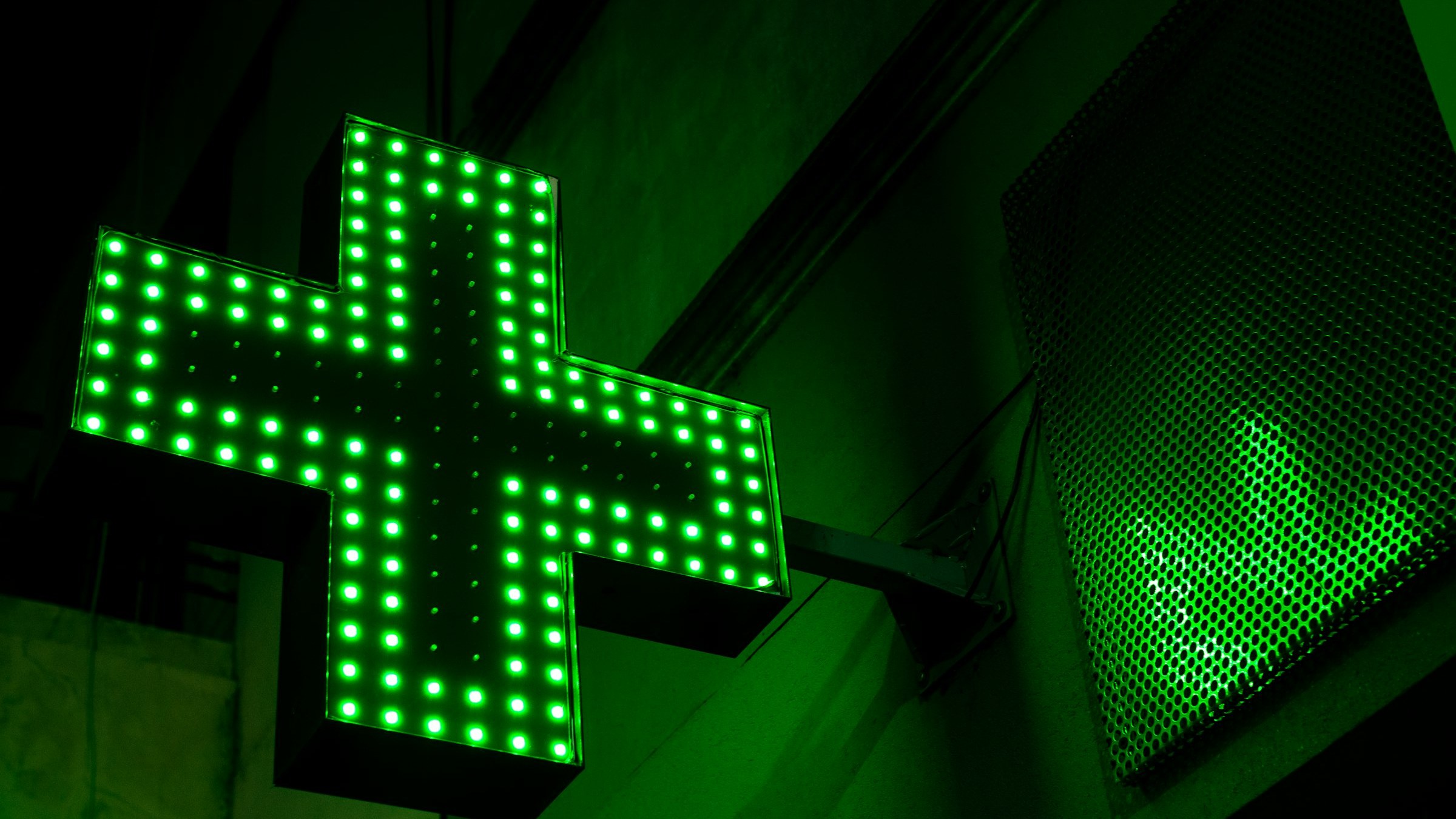 Illuminated green pharmacy cross sign on a building at night
