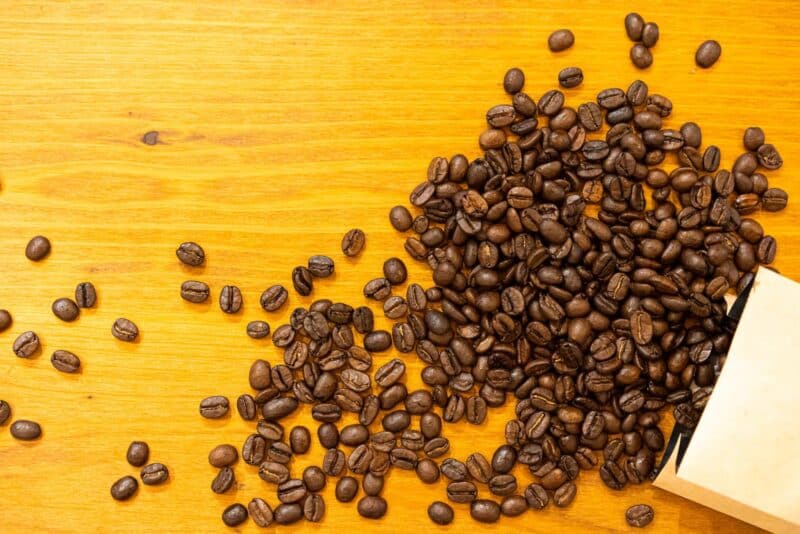 Freshly roasted coffee beans spilling from an unbranded bag onto a wooden counter