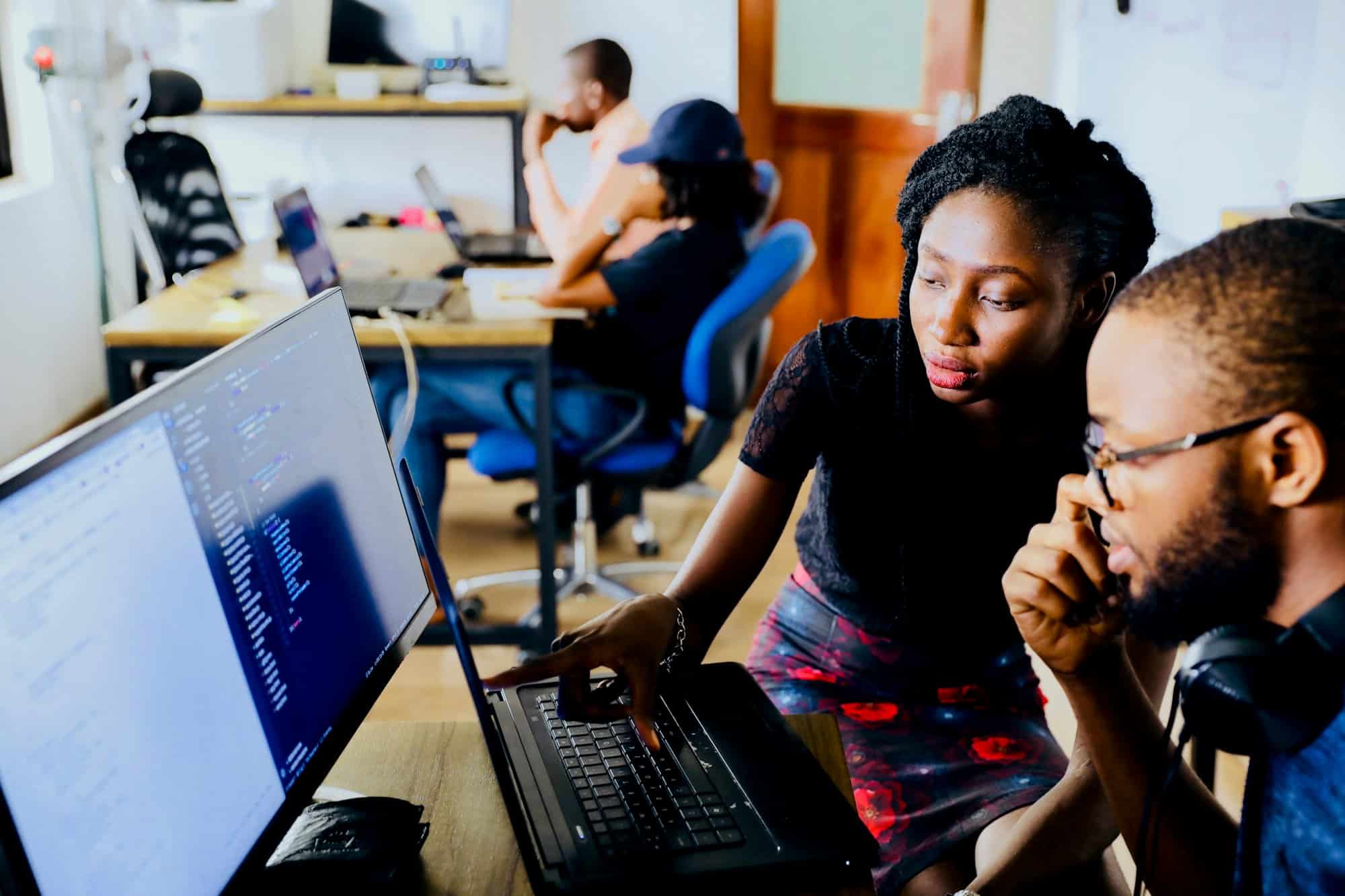 Two colleagues reviewing code on a laptop in a small office